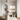 A framed landscape art print hangs on a beige wall in a styled interior room with a marble-top table, pink flower arrangements, a sculptural chair, and a spherical pendant light.