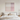 A minimalist bedroom scene featuring a large square abstract wall art print with soft vertical gradients of pink, beige, and white, hanging above a neatly made bed with white linens and neutral pillows.