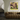 A framed abstract painting with green, purple, and yellow brushstrokes hangs on a beige wall above a brown boucle sofa in a modern living room setting.