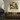 An abstract framed painting with green, pink, and purple brushstrokes hangs on a light gray wall above a brown textured sofa in a modern living room setting.