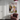 A framed abstract floral painting with pink, white, purple, and green brushstrokes hangs on a white wall in a modern room setting, next to a dusty rose velvet armchair and beneath a pink pendant light.