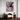 A framed abstract floral painting in shades of purple, pink, yellow, and green hangs on a white wall above a modern wooden armchair and a small round side table with a globe.